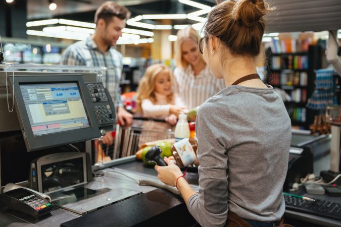 Supermarket cashier scanning groceries at the till for a smiling family with a full shopping trolley.